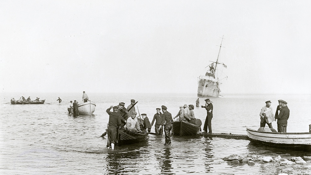 Sårade besättningsmän förs iland. I det grunda vattnet vadar Albatrossmän och ortsbor. Foto från Albatrossmuseets samlingar